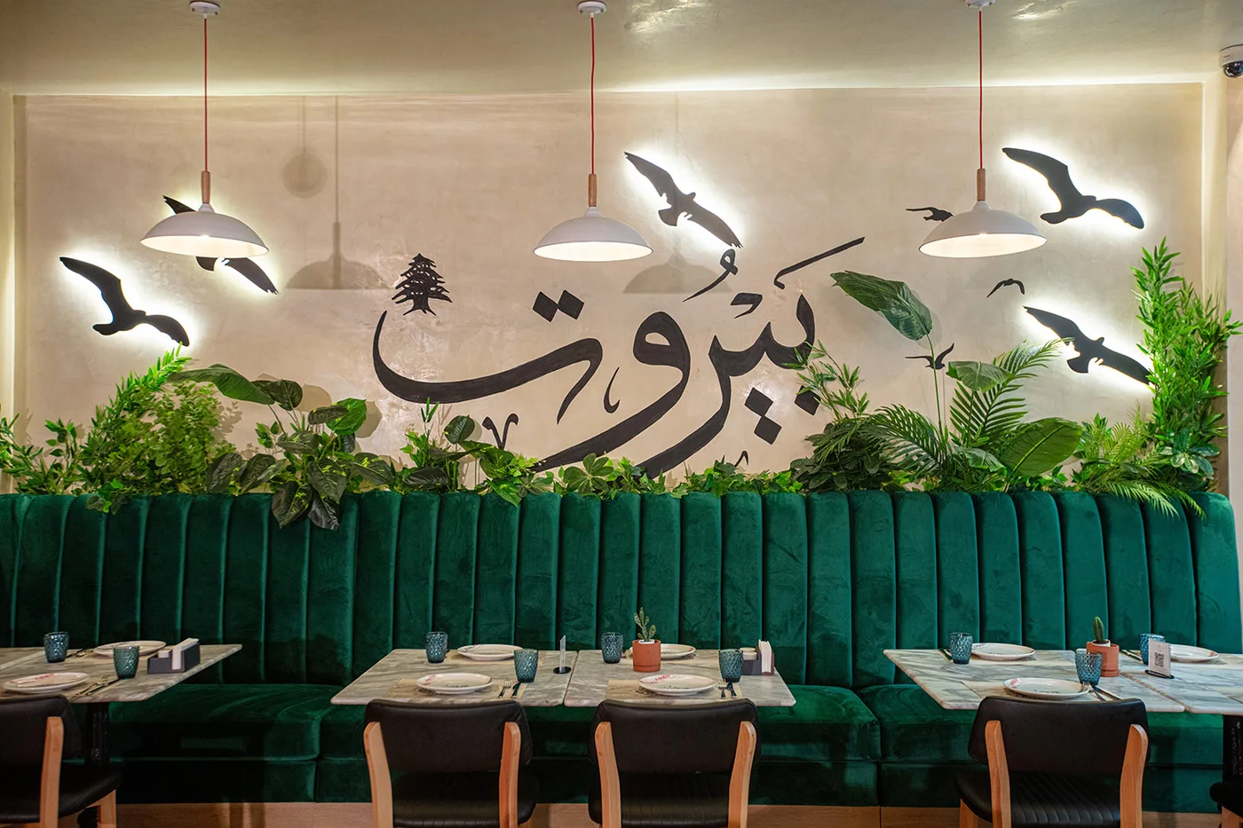 Habib Beirut Sofia dining room — green velvet booth seating beneath a Beirut Arabic calligraphy wall mural